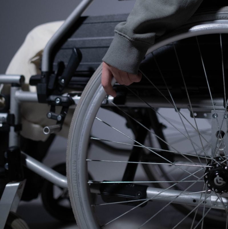 A detailed close-up shows a person's hand resting on a wheelchair rim, emphasizing disability and mobility aids.